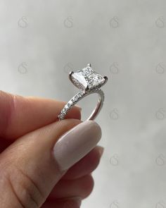 someone is holding their engagement ring with a princess cut diamond in the center and pave set diamonds on each side