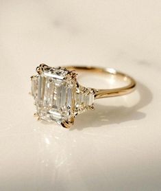 an emerald - cut diamond ring sits on a white surface