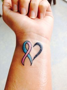 a woman's wrist with a pink and blue ribbon tattoo on her left arm