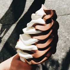 a hand holding an ice cream cone with chocolate and white icing