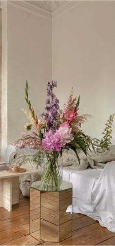 a vase filled with flowers sitting on top of a wooden table next to a bed