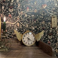 a clock sitting on top of a wooden table next to a candle and wallpaper