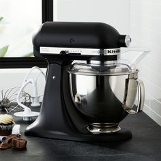 a black kitchen mixer sitting on top of a counter next to cupcakes and muffin tins