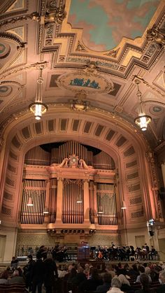 an auditorium filled with lots of people sitting in chairs and looking up at the ceiling