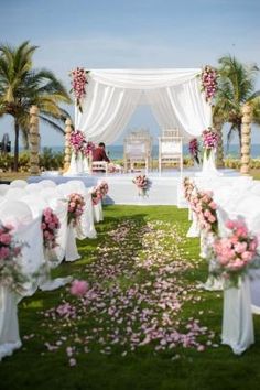 an outdoor wedding setup with white chairs and pink flowers on the grass at the end of the aisle