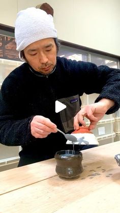 a man in a white hat is cutting something on a wooden table with a knife