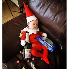 a baby dressed as an elf sleeping on a couch next to a bottle of wine