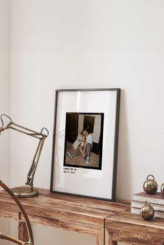 a framed photograph sitting on top of a wooden table next to a lamp and books