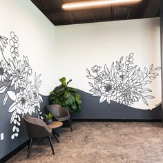 two chairs sitting in front of a wall with flowers painted on it