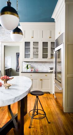 a large kitchen with white cabinets and wood flooring is pictured in this image, there are two stools at the center of the island