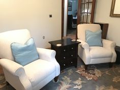 two white chairs sitting next to each other on a rug in a living room area