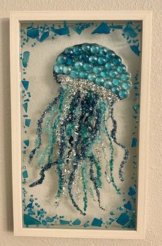 a blue and white jellyfish made out of beads in a frame on the wall