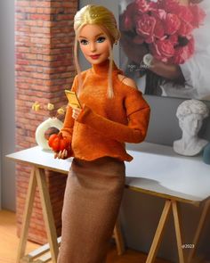 a barbie doll is standing next to a table holding a plate of tomatoes and carrots