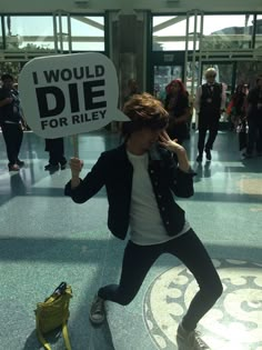 a woman holding a sign that says i would die for riley in the middle of an airport