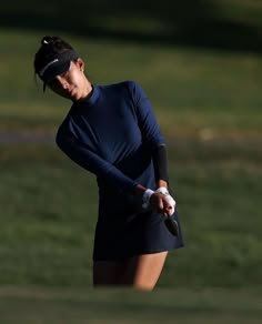 a woman holding a golf club in her right hand and wearing a blue shirt on the other side