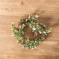 a wreath with red berries and green leaves sits on a wooden surface, ready to be used as an ornament