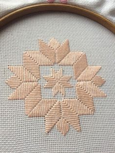 a close up of a cross stitch pattern on a piece of cloth with a wooden frame