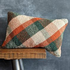 an orange, green and white pillow sitting on top of a wooden table next to a gray wall