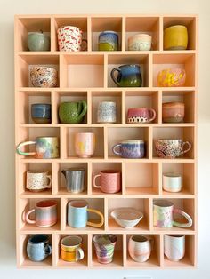 a wooden shelf filled with lots of different colored coffee mugs on it's sides