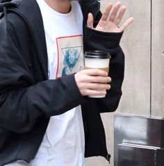 a young man holding a cup of coffee in his right hand and wearing a black jacket