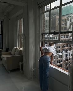 a woman standing in front of a window looking out at the city