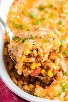 a spoon full of mexican casserole with meat and vegetables on it is being lifted from the casserole dish