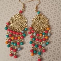 two pairs of colorful beaded earrings on a white tablecloth with gold chains and beads