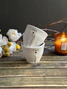 three white bowls sitting on top of a wooden table next to a candle and flowers