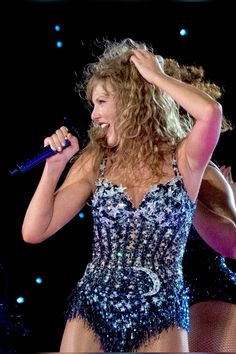 a woman in a bodysuit holding a microphone and singing into the air with her hands behind her head