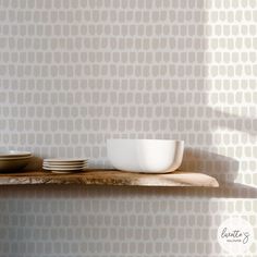 bowls and plates sit on a wooden shelf in front of a wallpapered background