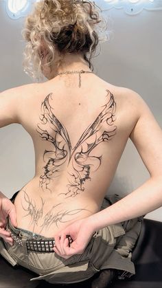 a woman with tattoos on her back holding a cell phone