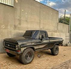 a black pickup truck parked in front of a concrete wall and brick floored parking lot