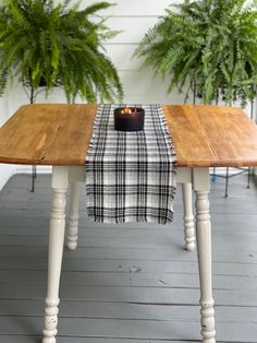 a wooden table topped with a black and white checkered table runner next to potted plants