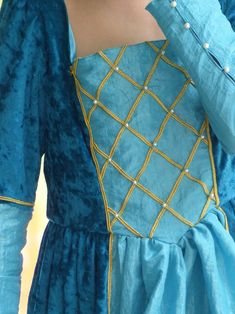 a close up of a person wearing a blue dress with gold threadwork on it