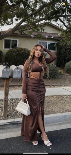 a woman standing in front of a house wearing a brown skirt and cropped top