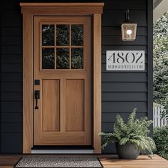 a wooden door on the side of a black house next to a potted plant