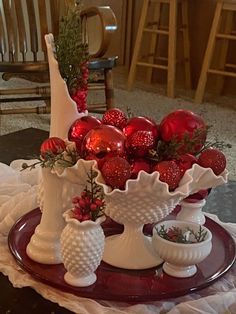 red and white christmas decorations sit on a table in front of a glass vase filled with strawberries