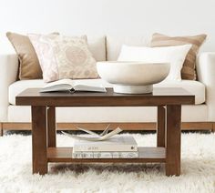 a coffee table with books on it in front of a white couch and pillowed area