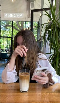 a woman sitting at a table with a drink in front of her and cell phone