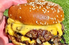 a hand holding a cheeseburger on a bun with meat, onions and cheese