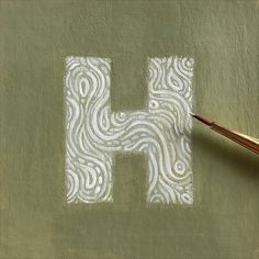 the letter h is drawn with white paint on a green surface next to a brush