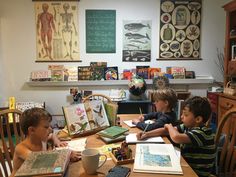 three young boys sitting at a table with books and notebooks on top of it