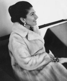 black and white photograph of woman in fur coat sitting at piano looking off to the side