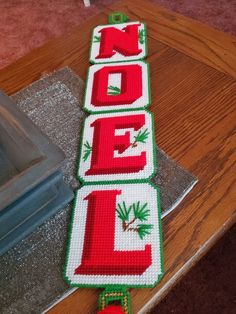 a cross stitch christmas sign on top of a wooden table with the word noel spelled out in red and green