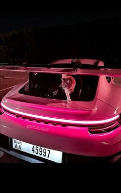 a pink car parked in a parking lot at night with its hood up and the lights on