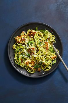 a black plate topped with pasta and broccoli on top of a blue table