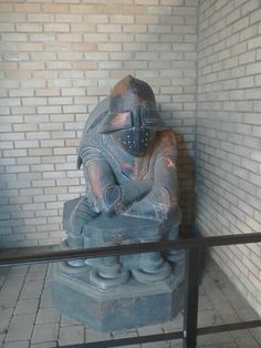 a statue in the corner of a room with bricks on the wall and a metal fence around it