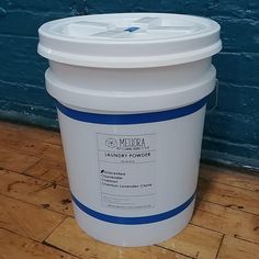 a white bucket sitting on top of a hard wood floor next to a blue wall