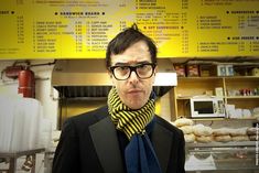 a man wearing glasses and a tie standing in front of a food court with menus on the wall