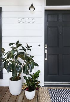 two potted plants sit on the porch next to a black door and white wall